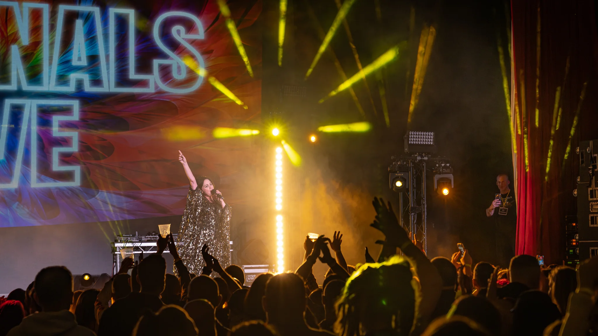 Singer performing under warm show lighting as the audience raises their hands
